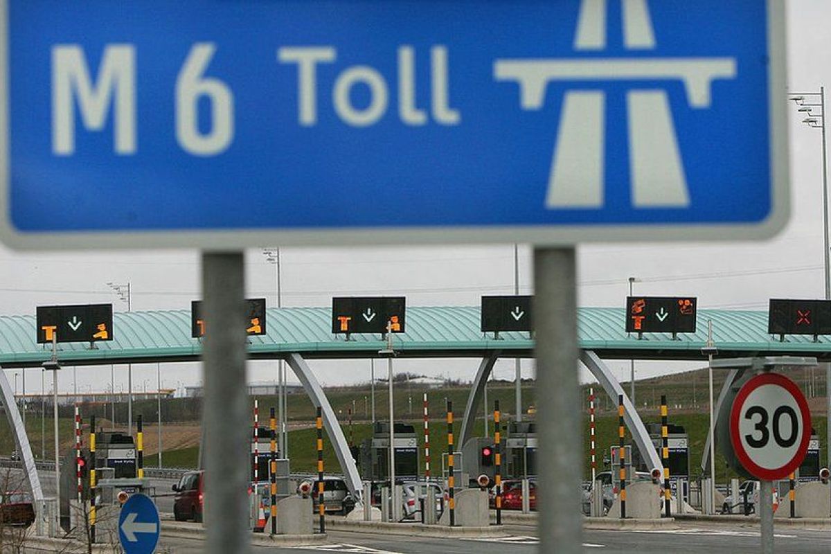 A man in a blue shirt and tie sitting in the driver's seat of a lorry, backing up.