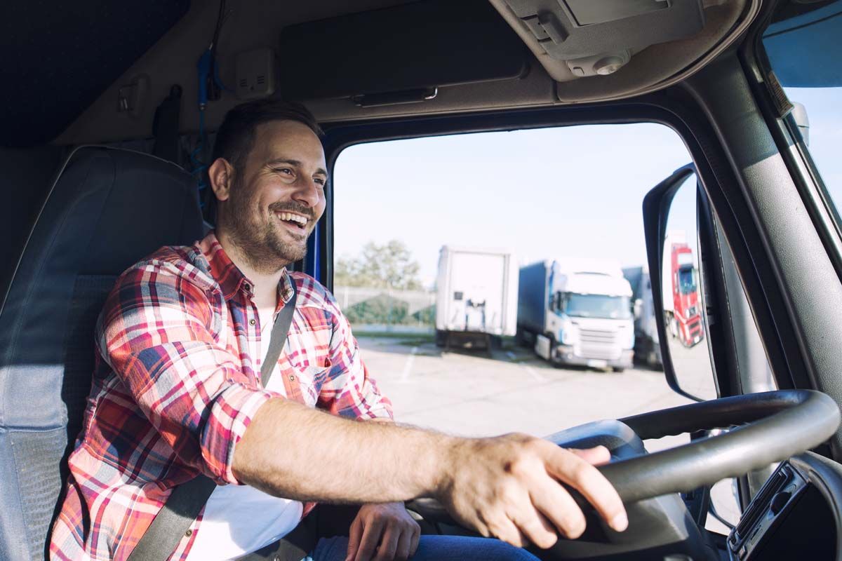 A man with a cheerful expression drives a truck, radiating happiness and confidence on the road.