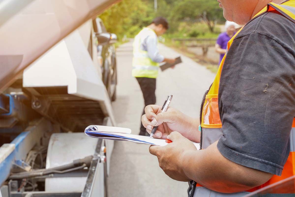 A man in a safety vest writes on a clipboard while standing next to a lorry