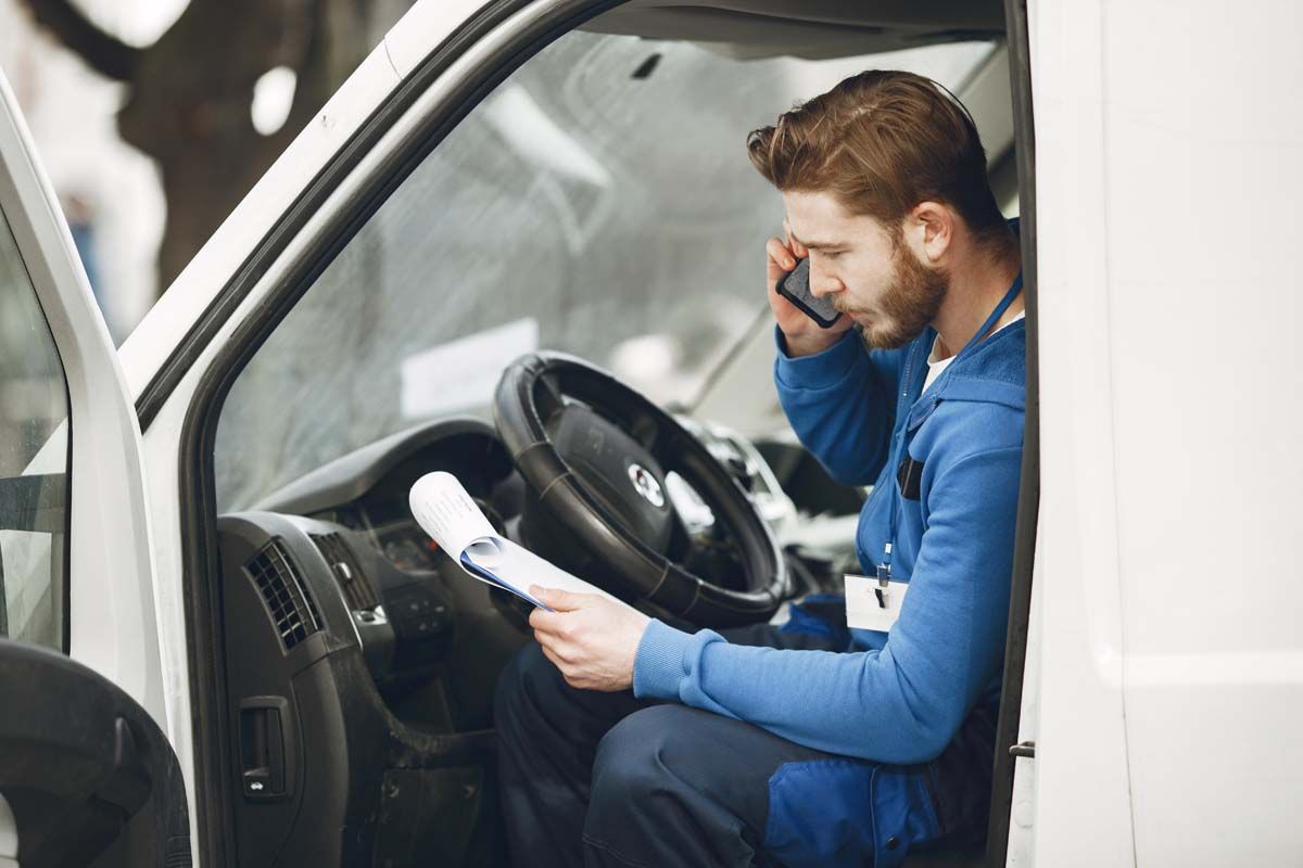 A man in the driver's seat of a van, talking on the phone.